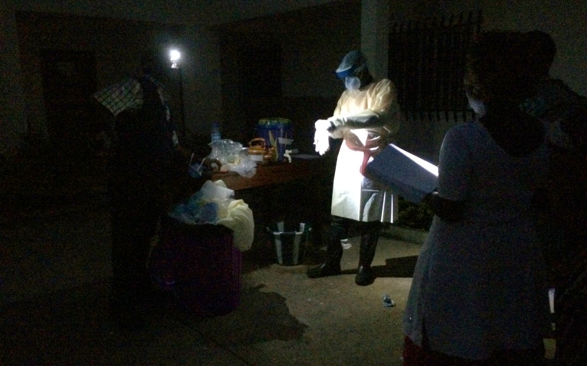 Healthcare worker in full protective equipment putting on gloves at night during the 2014 Ebola outbreak in Guinea