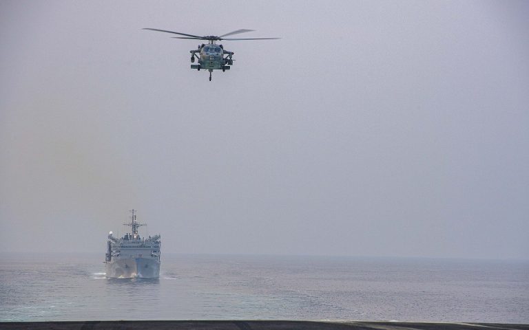 A U.S. Navy helicopter flies over the Strait of Hormuz with a Navy supply ship behind it