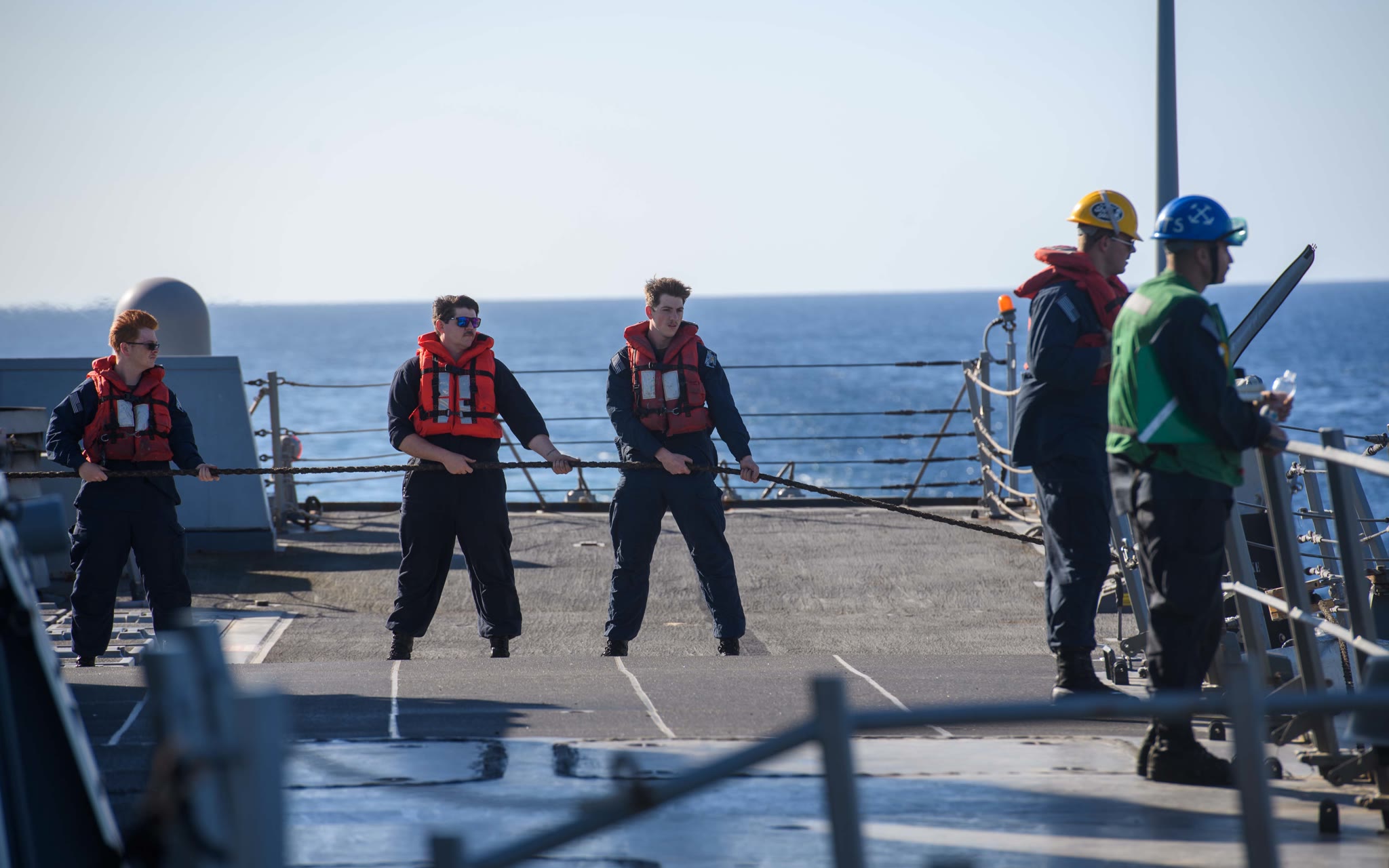 U.S. Navy sailors in life vests haul a refueling line across the deck of the destroyer USS Mason during a replenishment-at-sea in the Red Sea